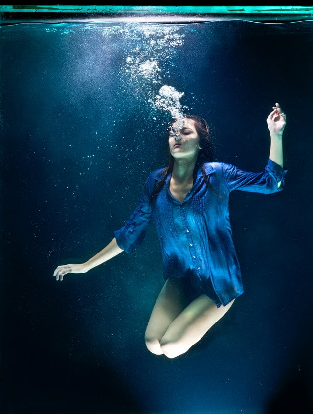 Woman underwater in tank represents emotional healing with Pluto Moon and dream work.